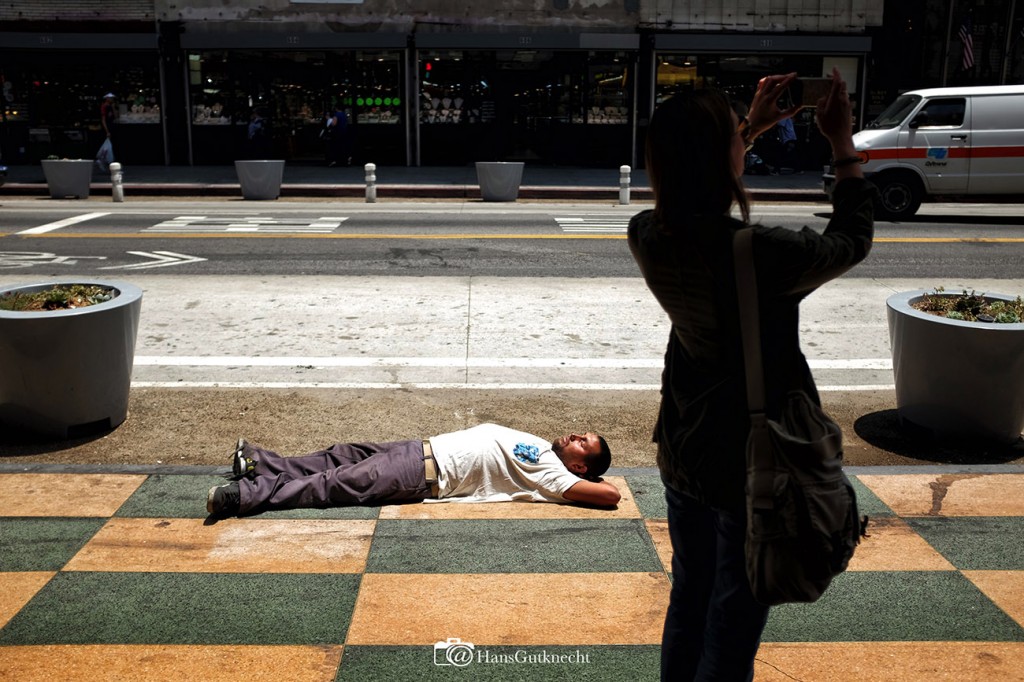 A woman takes a photos as a man takes a nap along S. Broadway in Los Angeles Wednesday, May 27, 2015.  (Photo by Hans Gutknecht/Los Angeles Daily News)